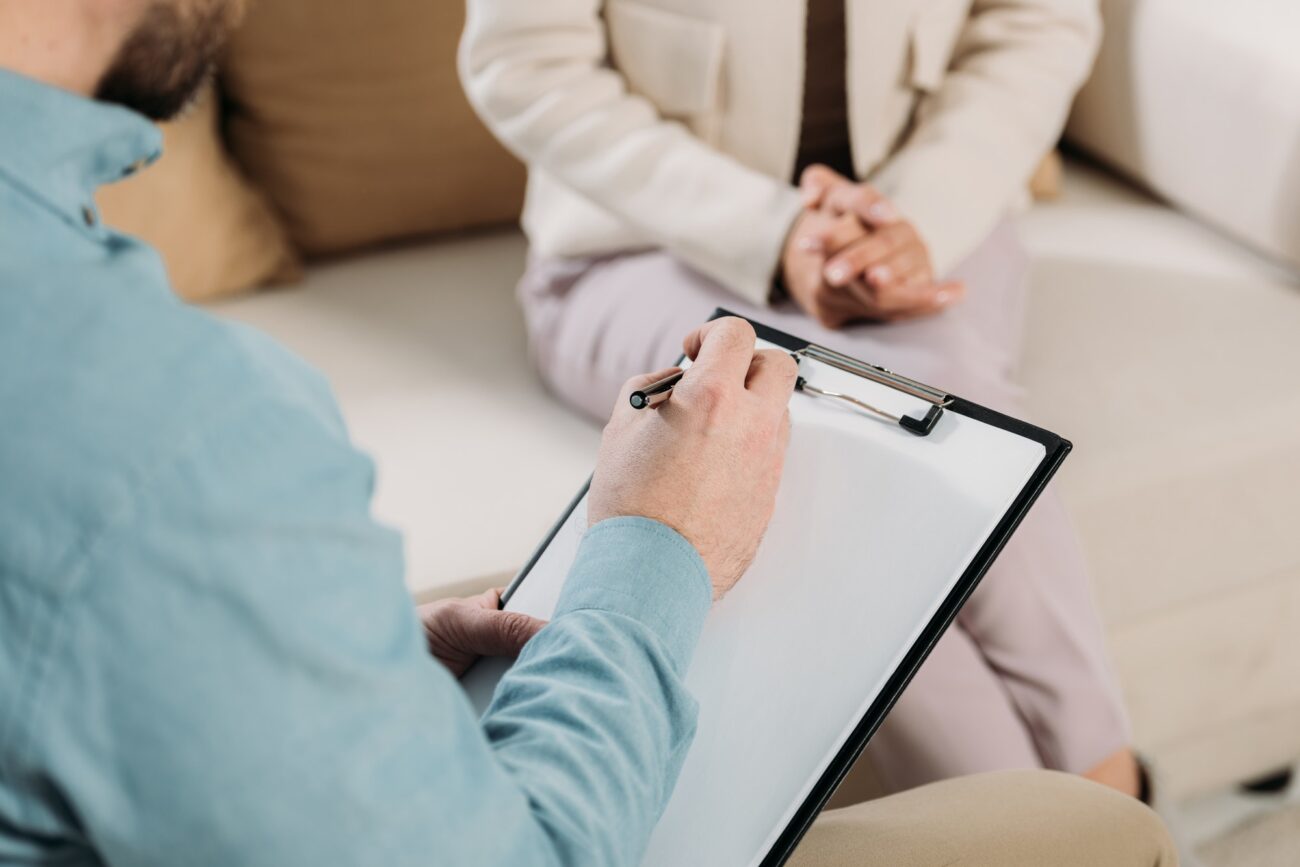 cropped shot of psychotherapist writing on clipboard and female patient sitting on couch